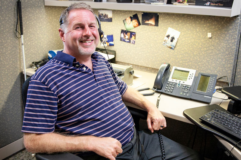 Alan smiling wearing headset with phone and laptop