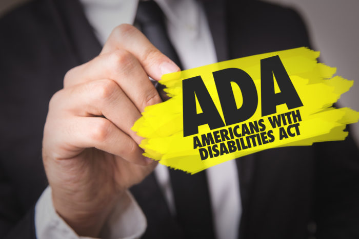 Man in suit holding small sign that says ADA Americans With Disabilities Act