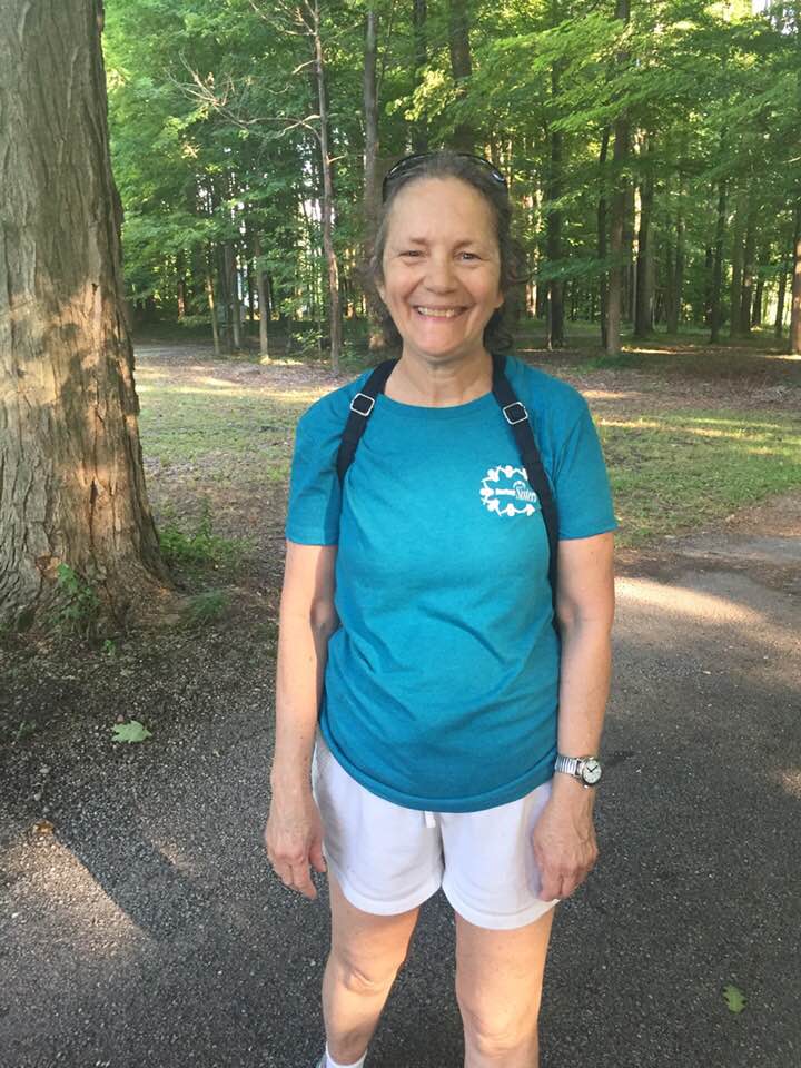 Amy smiling and standing on path in park wearing her "Daring Sisters" turquoise t-shirt 