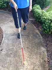 person walking on sidewalk using white mobility cane 