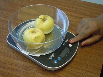 talking food scale with bowl of yellow apples on it. finger points to the controls