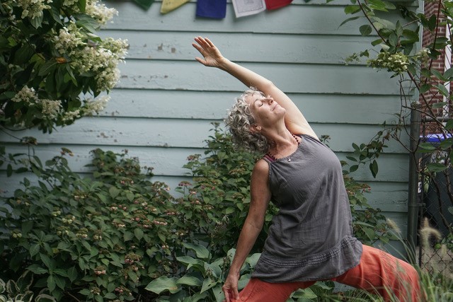 Pictured: woman wearing loose clothing, outside in the grass doing a yoga pose.