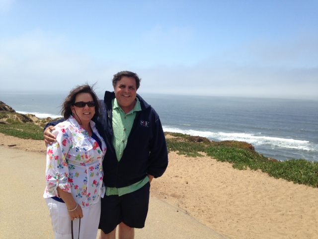 husband and wife standing on beach. he has his arm around her.