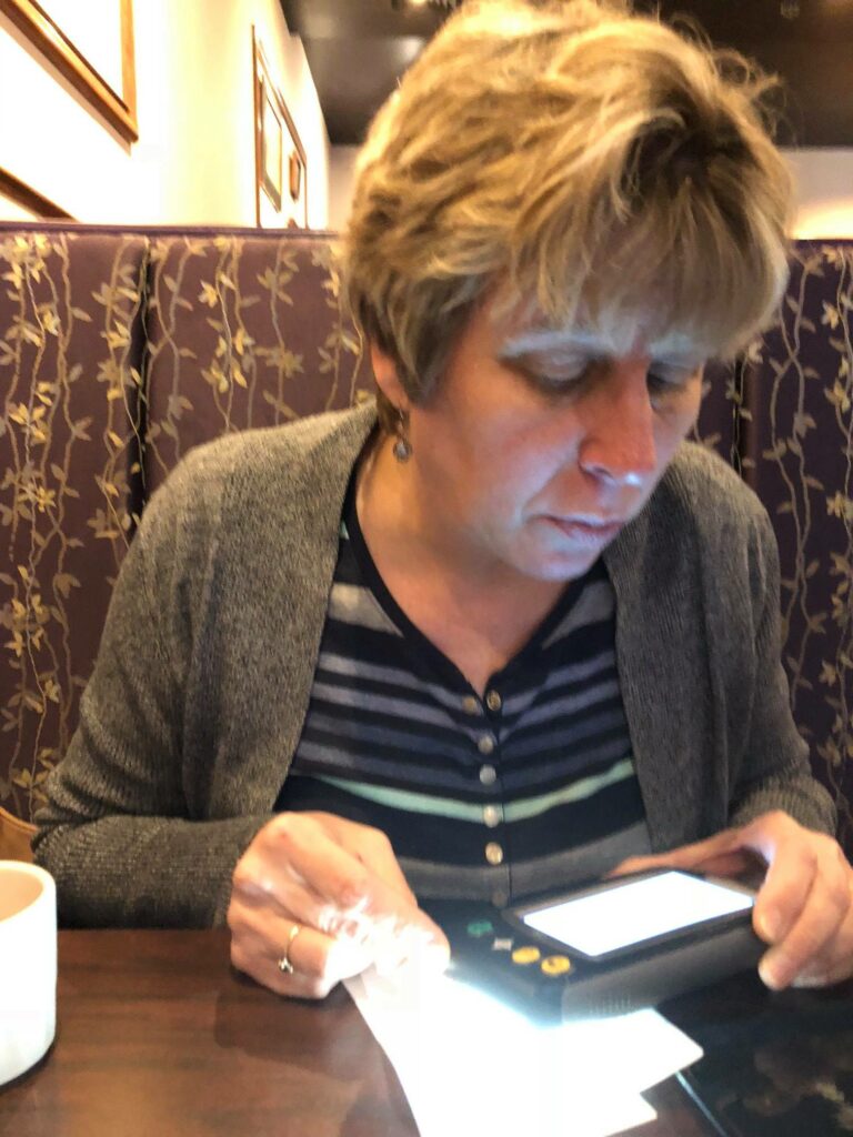 Beckie reading menu at restaurant with hand held video magnifier