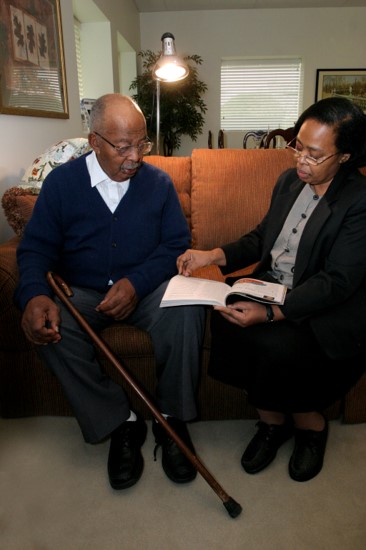 older man sitting next to daughter on couch. She is reading to him.