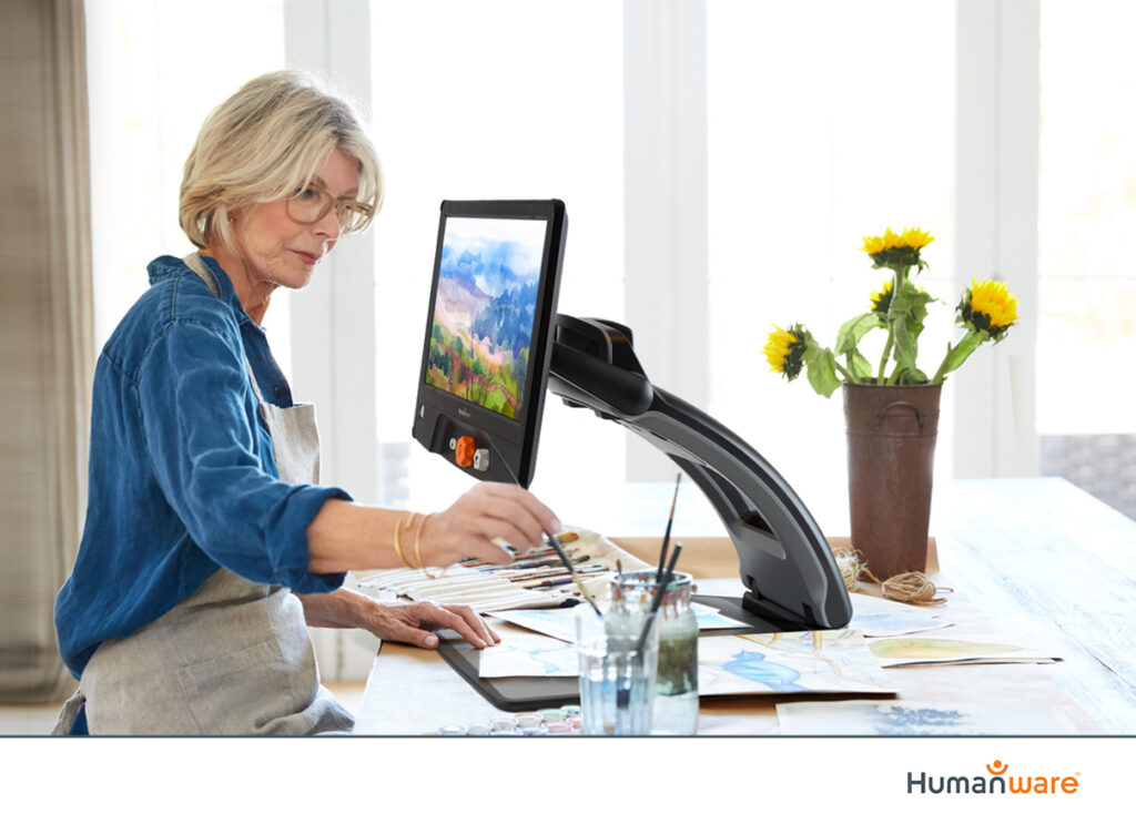 woman painting and viewing image on a large desktop magnifier