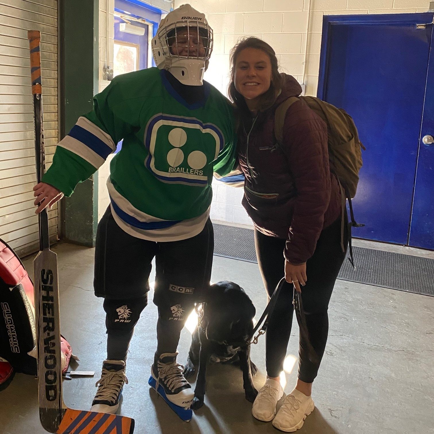 Liz Bottner dressed in hockey gear, her guide dog Guiding Eyes Ocala, and  Ocala's puppy raiser Samantha Epstein