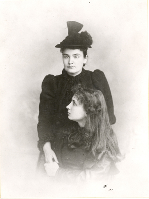 Anne Sullivan standing behind a young Helen who is sitting. 