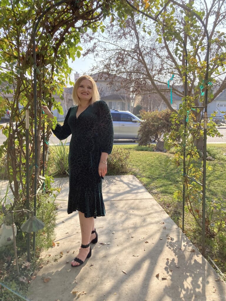 Marana, a woman with blond hair wearing a blue dress, is posing on a sidewalk