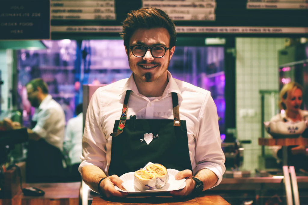 Photo of a man wearing an apron holding a plate of food.