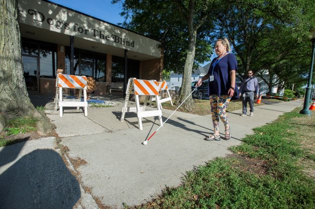 Woman with white cane outstretched, walking down sidewalk