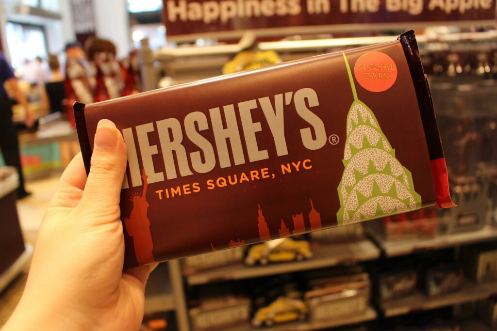 Hand holding Hershey bar. Bar says Times Square, NYC and has an image of Manhattan skyline. Photo by Janne Simoes on Unsplash