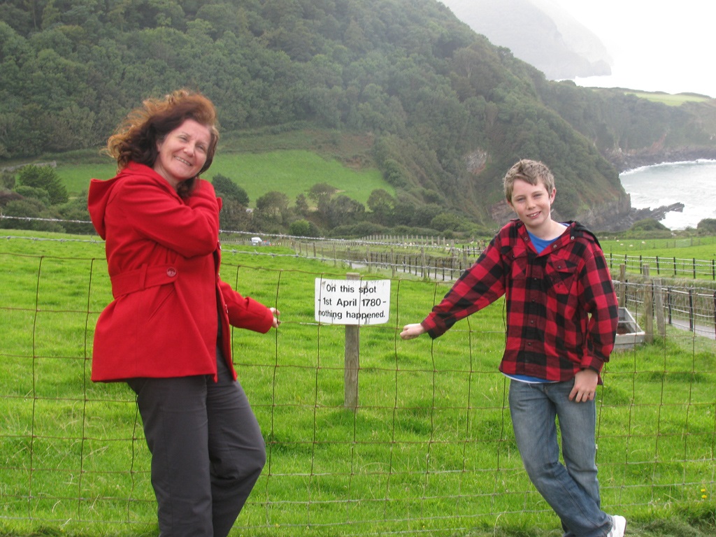 Maribel and son standing on a hill in front of a fence behind which is a sign that says " On this spot in April 1780 nothing happened."