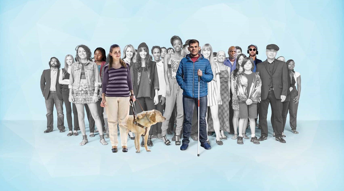 A black and white photo with a light blue background with a diversified group of about 25 people of all different ethnicities, ages, genders and styles of clothing.  A few people are in color including a young woman in the front of the group with her guide dog, a man holding a white cane and a man wearing headphones.  Photo provided by HKNC National Center